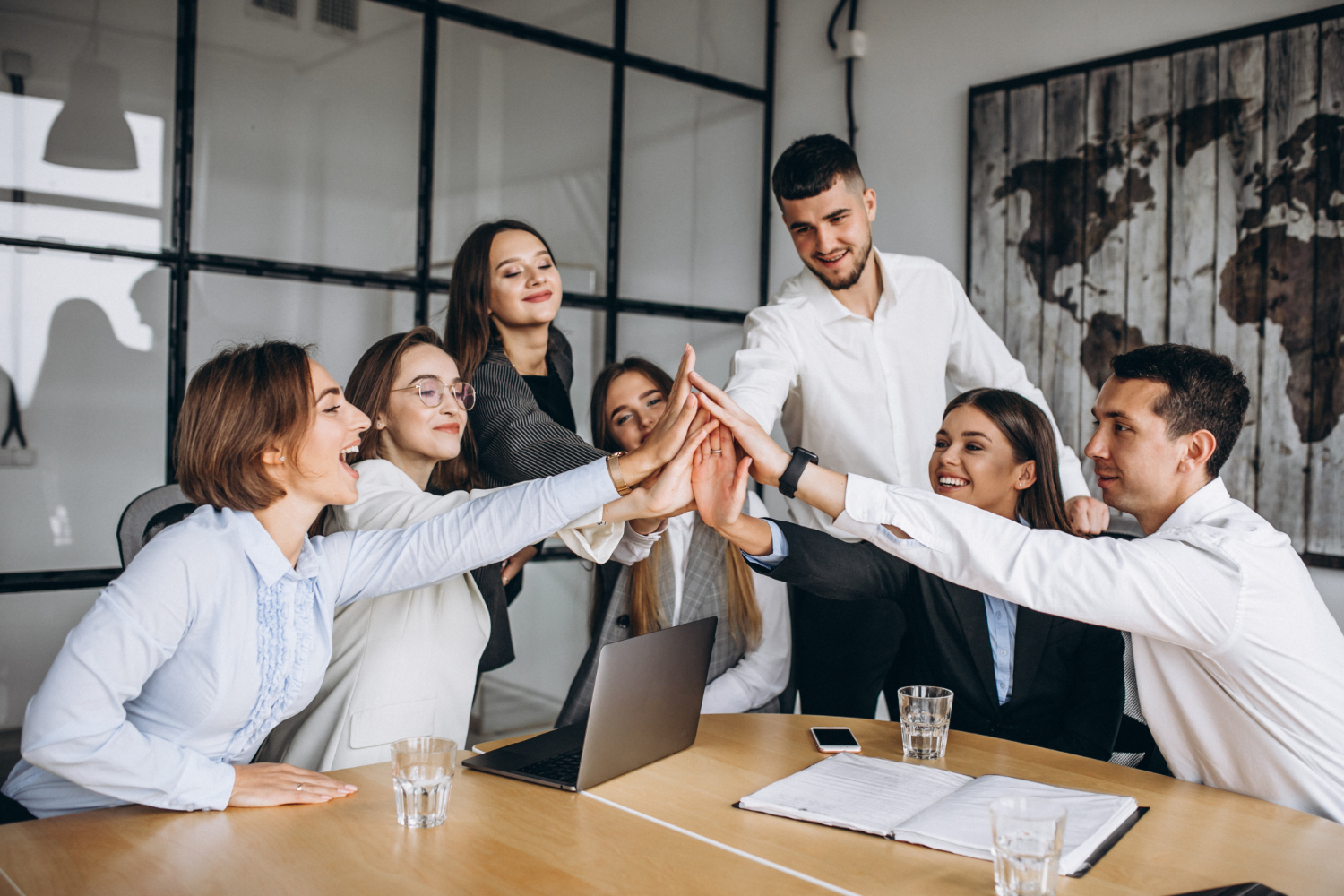 Grupo de profissionais de negócios celebrando a colaboração e sucesso com um 'high five' em uma reunião de equipe em um escritório moderno.